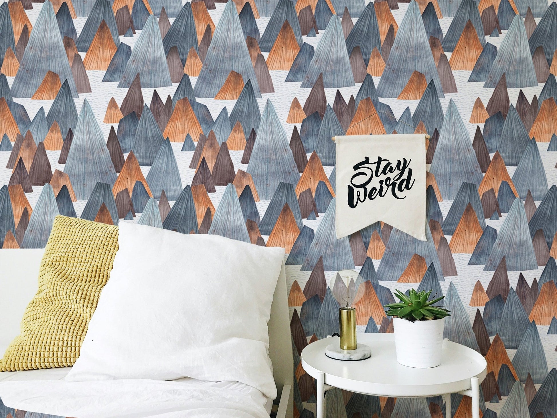 Blue and grey mountain wallpaper behind white pillows and yellow throw.