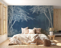 Indigo forest wall mural in a bright bedroom with beige linens and a side table.