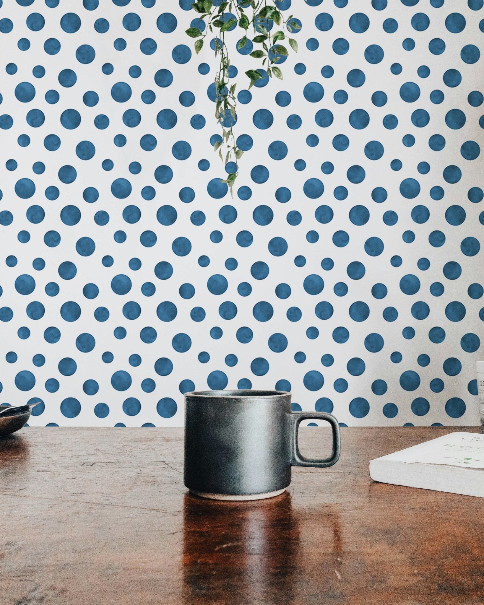 Hand-painted indigo dot wallpaper shown with a coffee mug on a wooden table.