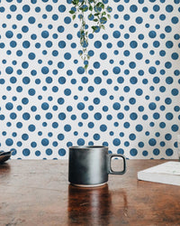 Hand-painted indigo dot wallpaper shown with a coffee mug on a wooden table.