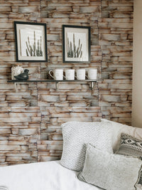 Sandstone wallpaper behind a bed with framed botanical art on the wall.
