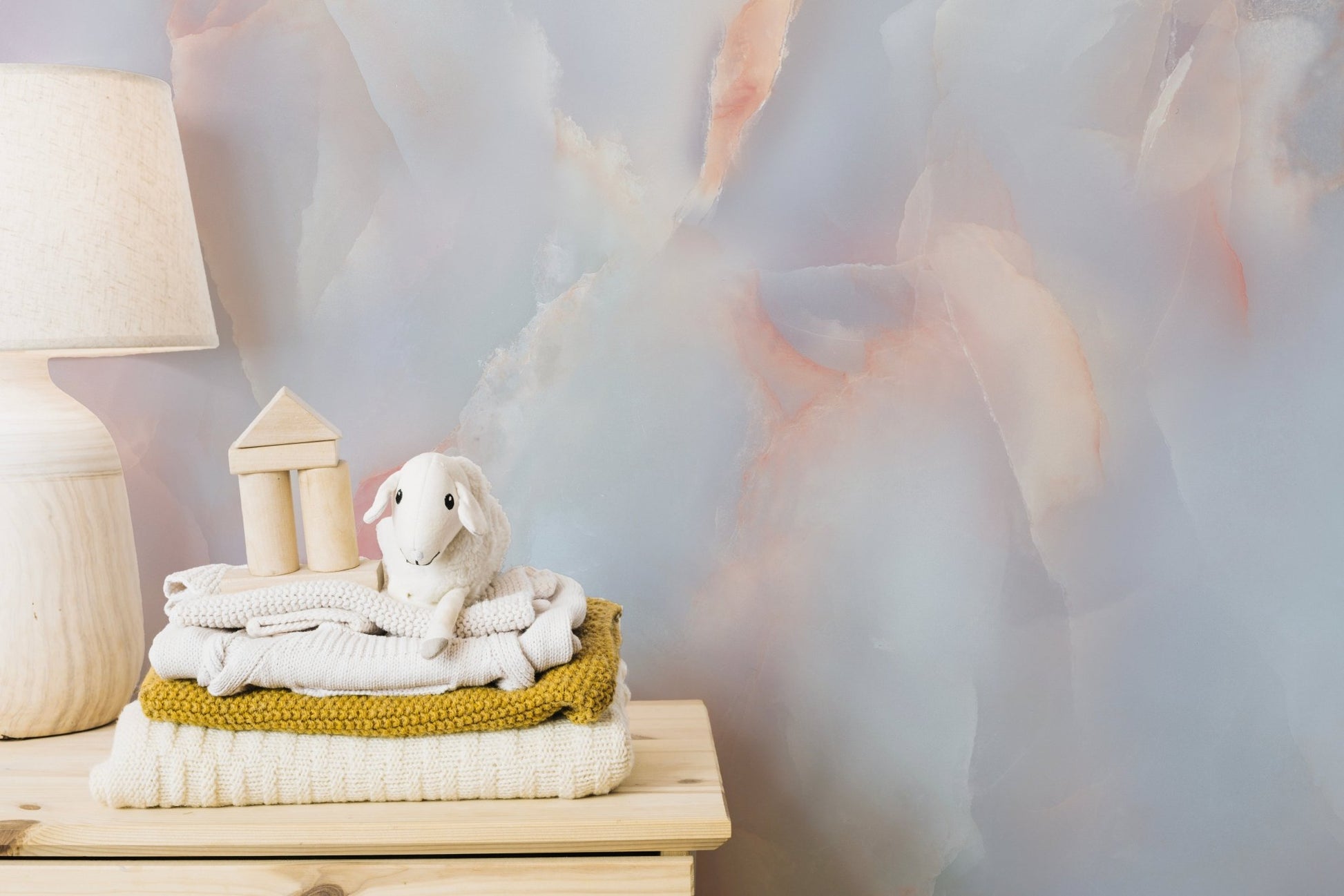 Soft pink and blue marble wall mural in a nursery with a white changing table.