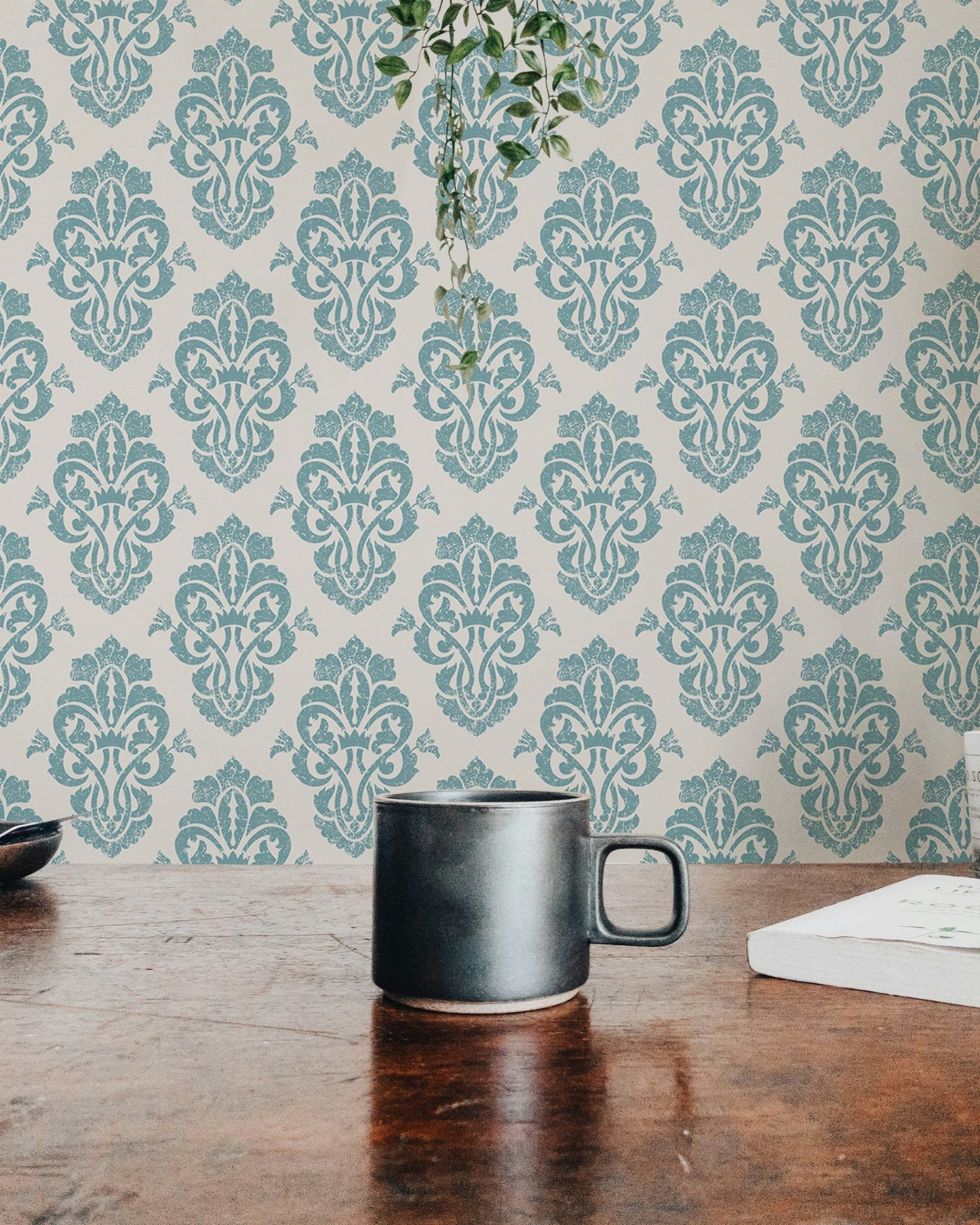 Teal damask wallpaper behind a coffee mug on a wooden desk.