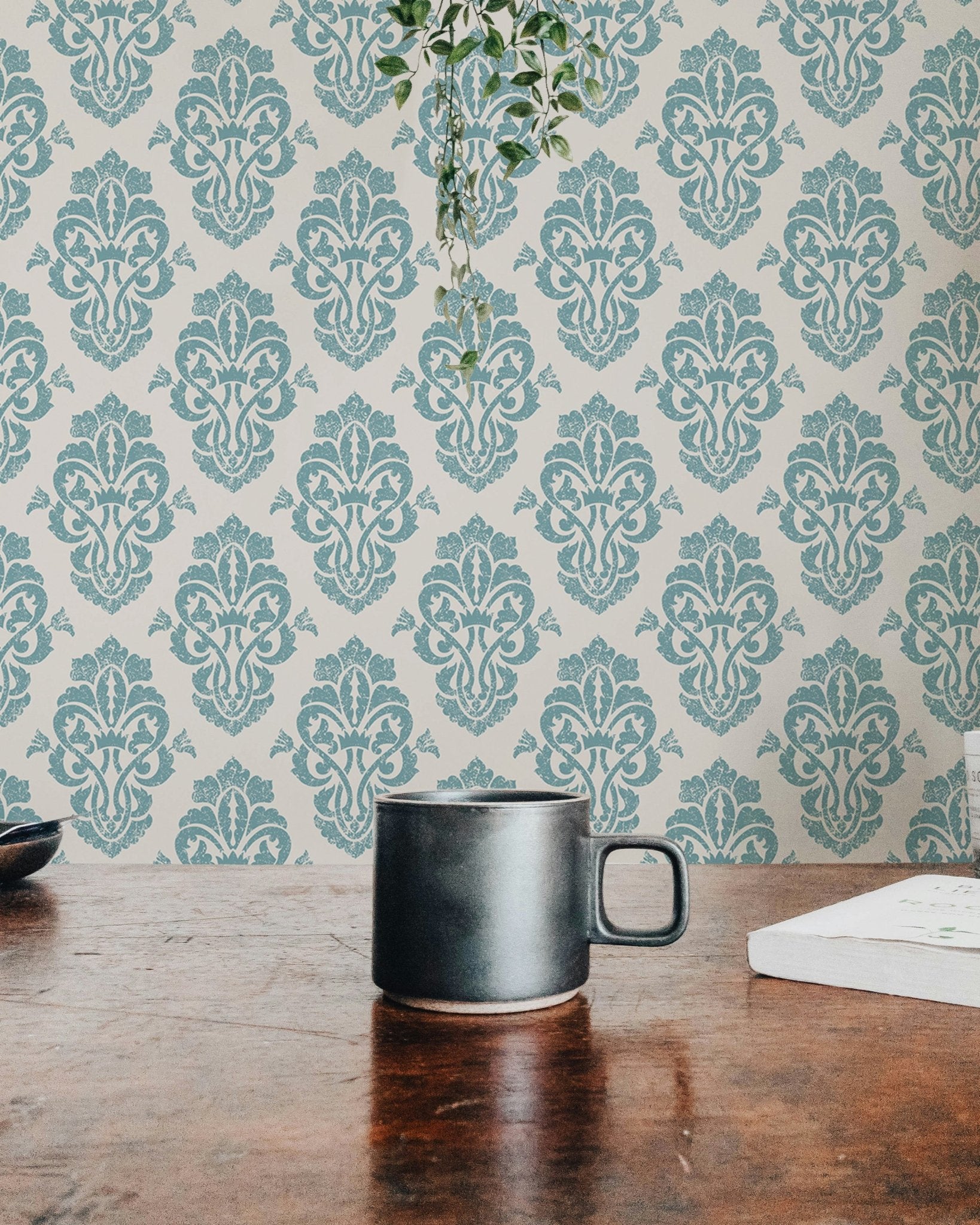 Teal damask wallpaper behind a coffee mug on a wooden desk.
