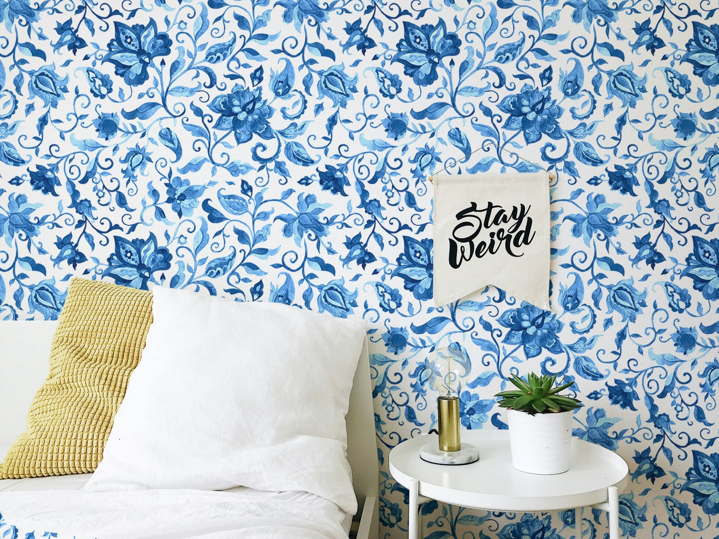 Bedroom wallpaper featuring watercolor flowers behind white bedding and yellow pillow.