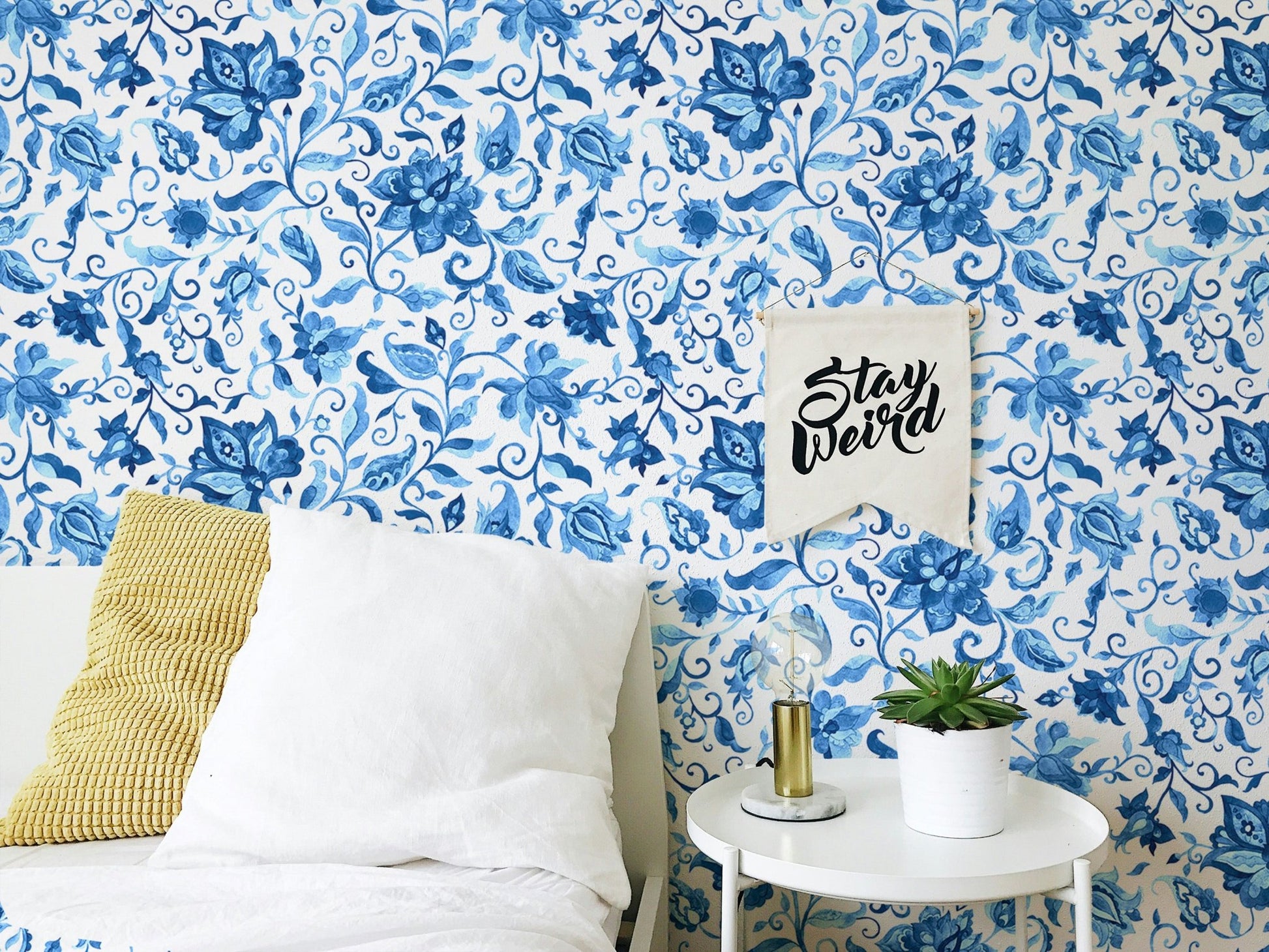 Bedroom wallpaper featuring watercolor flowers behind white bedding and yellow pillow.