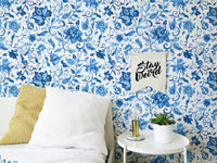 Bedroom wallpaper featuring watercolor flowers behind white bedding and yellow pillow.