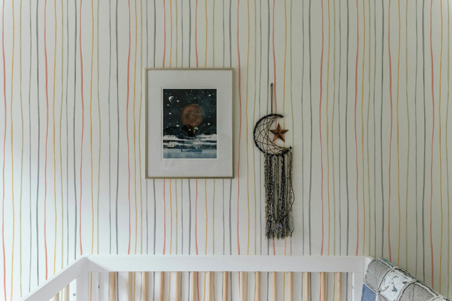 Vertical pastel striped wallpaper behind a white baby crib