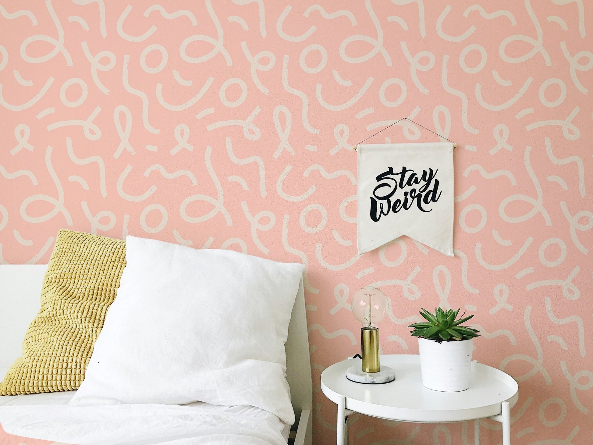 Pink line brush stroke wallpaper behind a bed with white and yellow pillows.