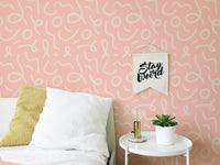 Pink line brush stroke wallpaper behind a bed with white and yellow pillows.