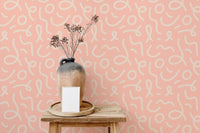 Peach pink wallpaper with white swirl patterns behind a vase on a wooden stool.