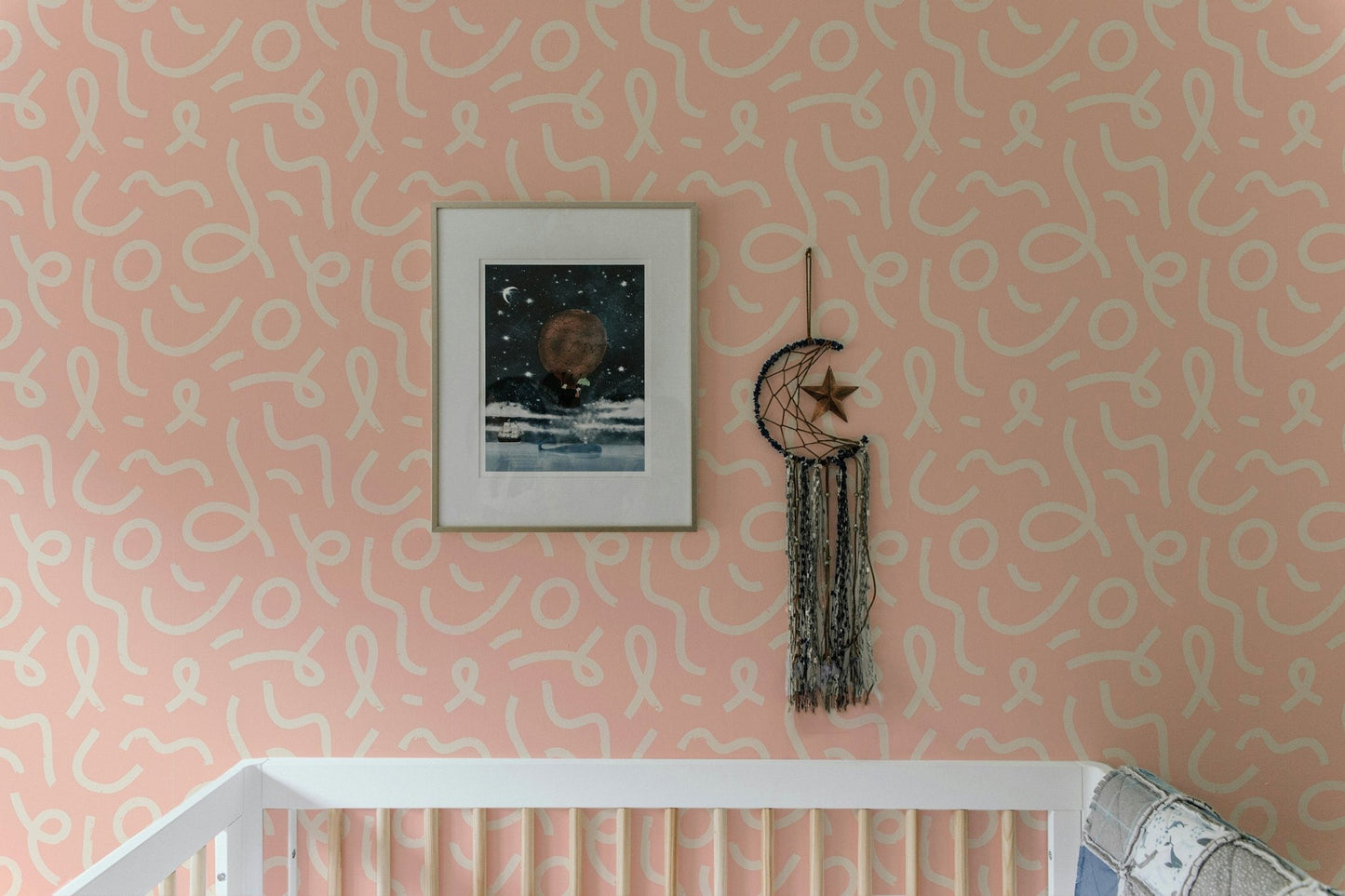 Abstract line wallpaper in a nursery above a wooden cot and framed art.