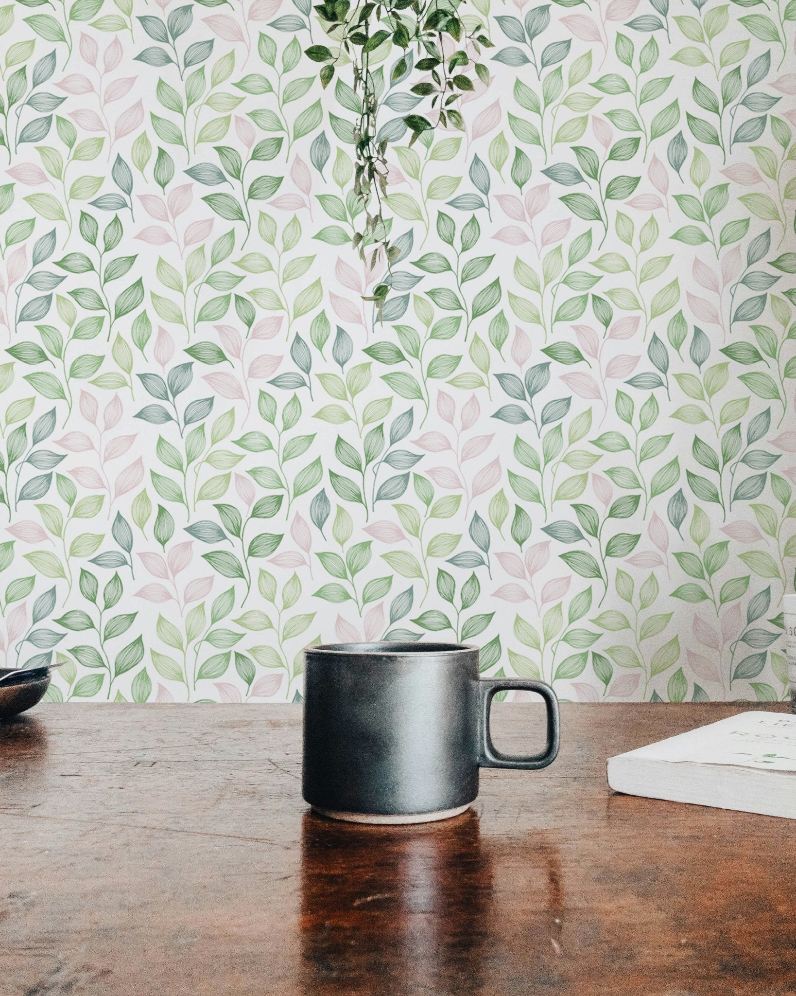 Wallpaper with small green and pink leaves behind a dark coffee mug on a table.