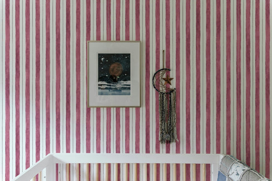 Pink and white vertical striped wallpaper behind a white wooden crib.