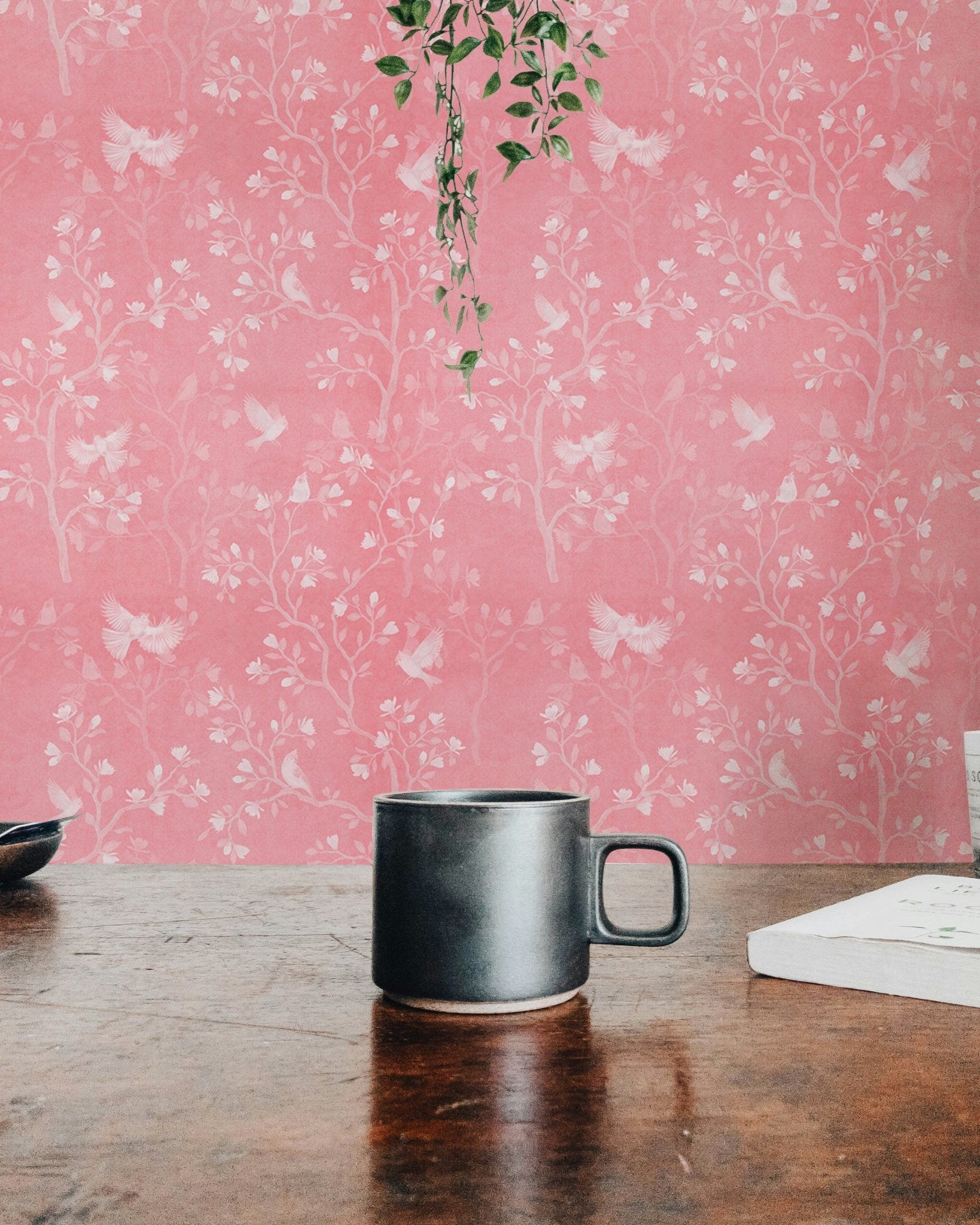 Pink botanical wallpaper on a feature wall near a wooden desk and mug.