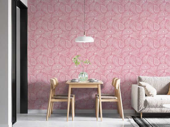 Pink hand drawn paisley wallpaper in a dining space with light wood chairs.