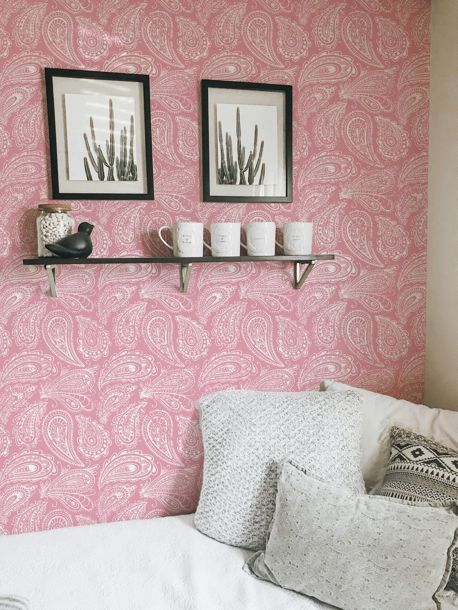 Wallpaper with pink ornament pattern behind a grey sofa and black frames.