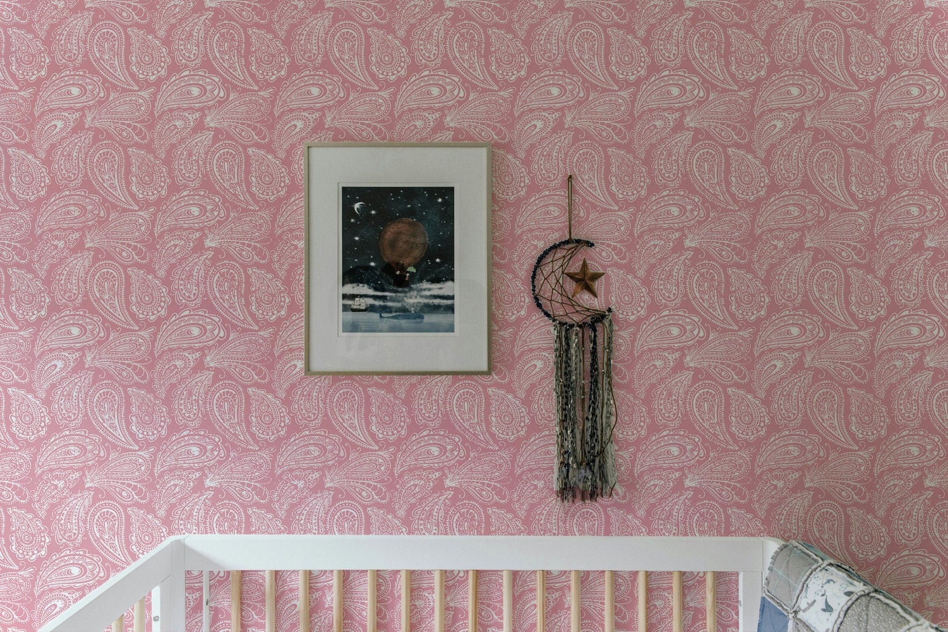 Decorative pink ornament wallpaper in a nursery with a framed mountain print.