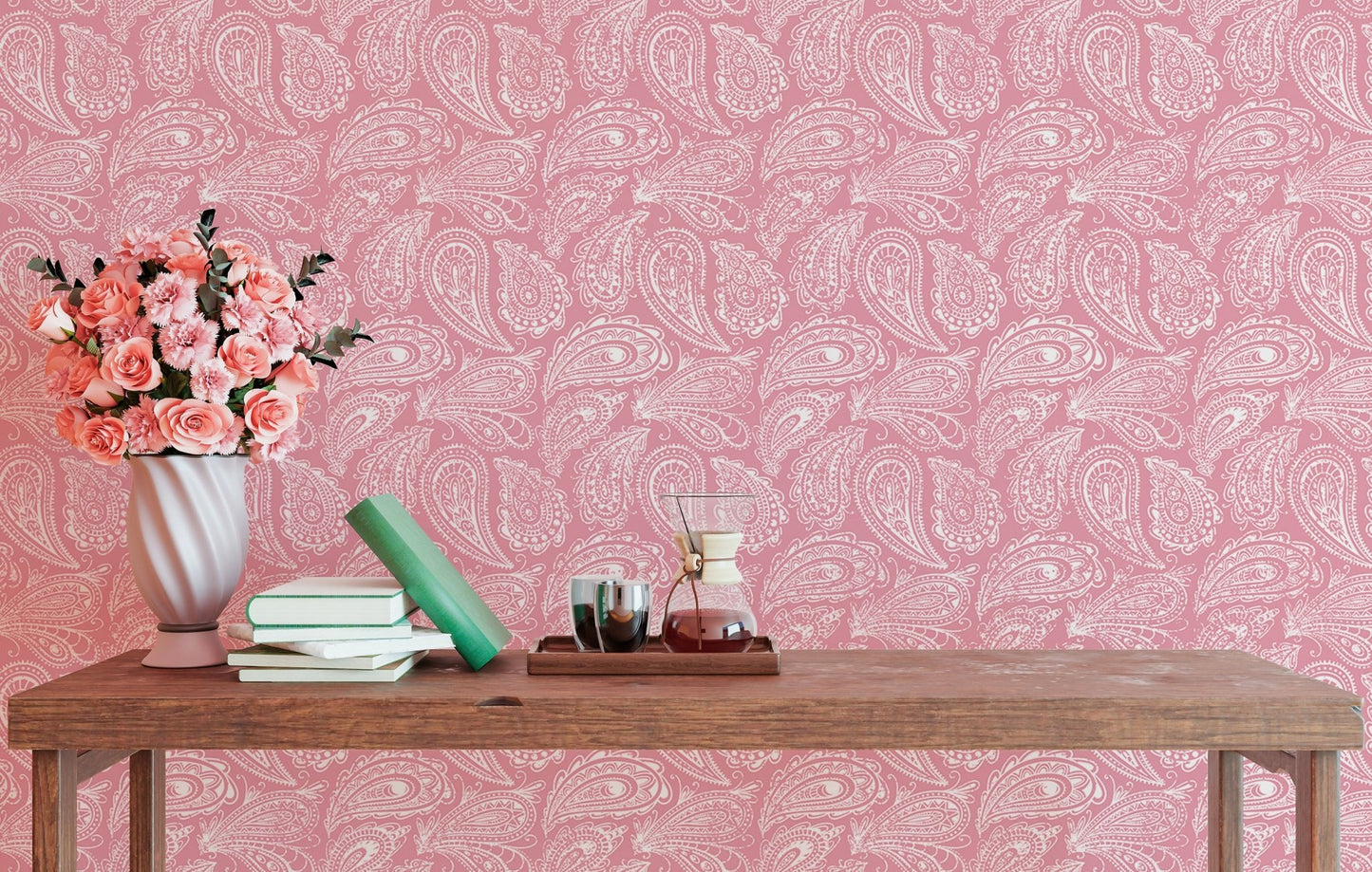 Pink wallpaper with paisley design behind a console table and flower vase.