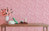 Pink wallpaper with paisley design behind a console table and flower vase.
