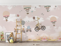 Nursery wall mural with a giraffe, bicycle, and hot air balloons on a pink background.