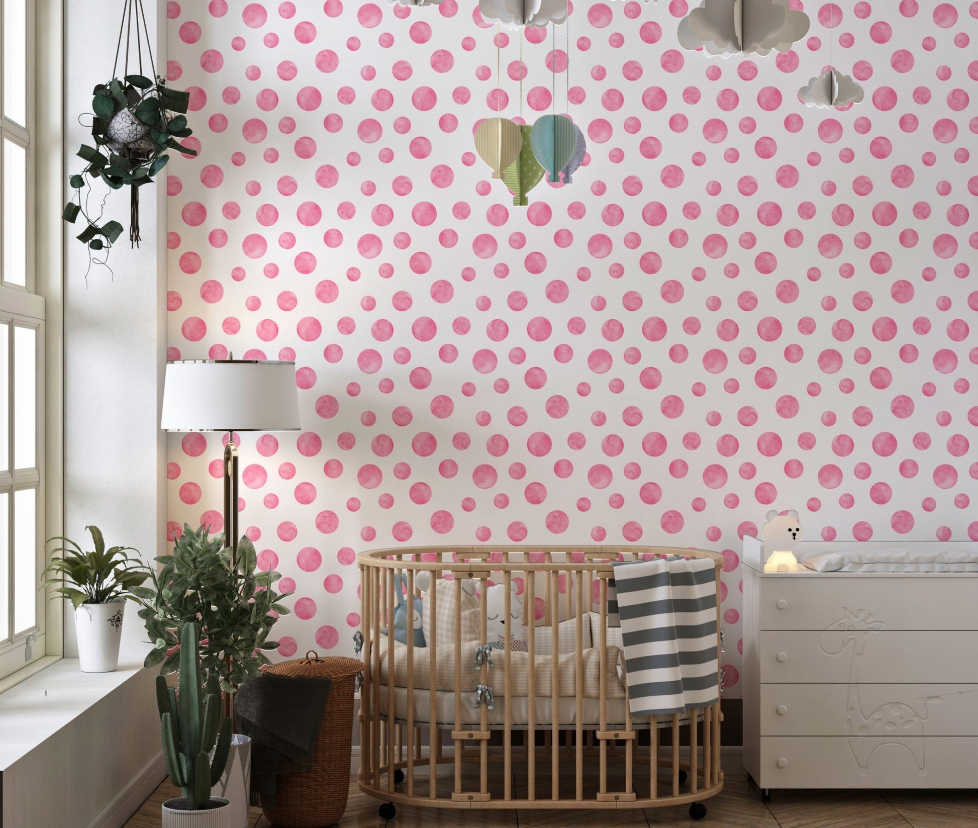 Pink polka dot wallpaper in a nursery with a wooden crib and white lamp.