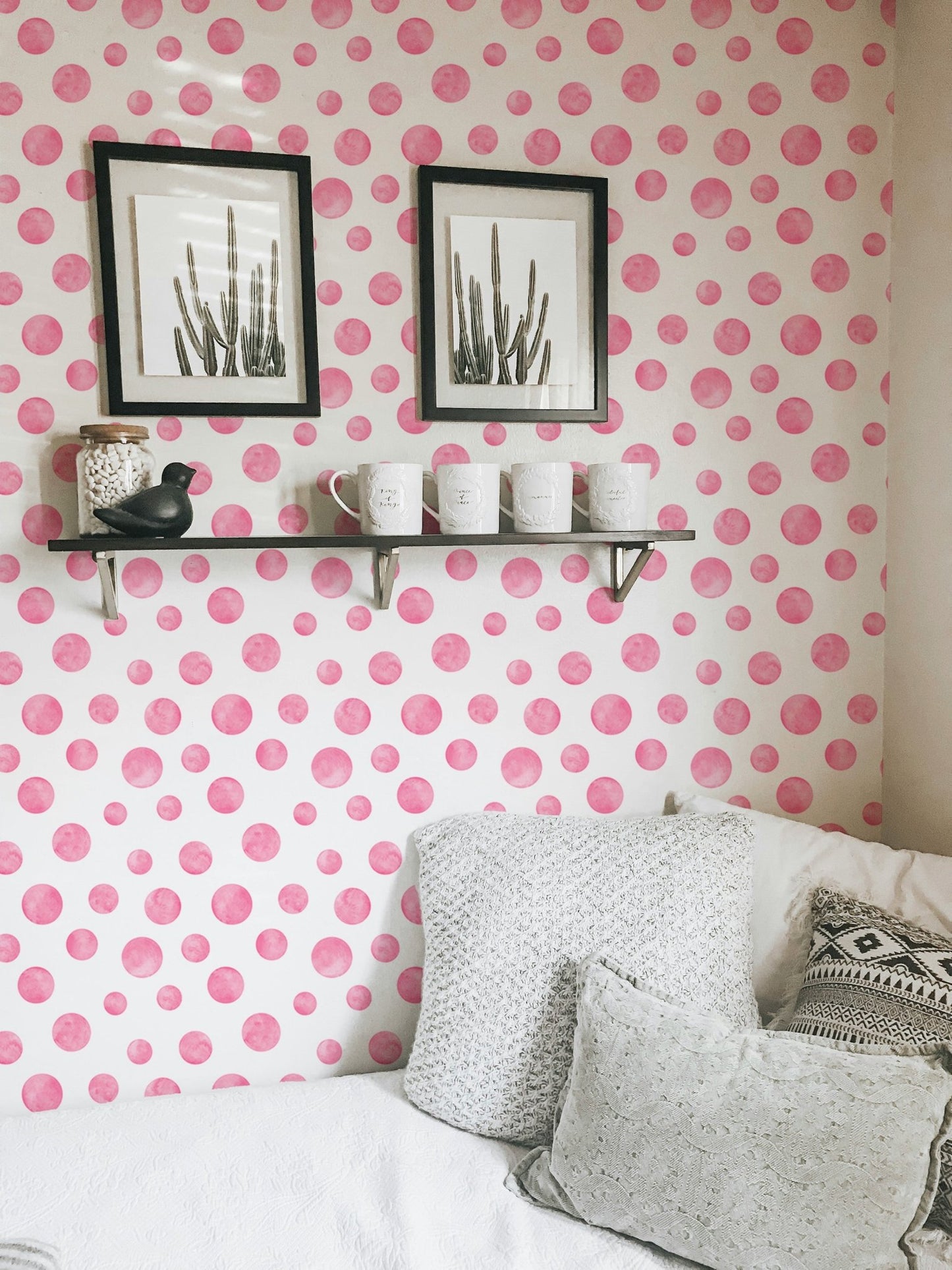 Pink circular pattern wallpaper in a bedroom with white pillows and black frames.