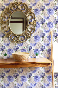 Round gold mirror mounted on a purple floral watercolor wallpaper in bathroom.