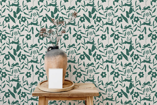 Green floral wallpaper with rabbits behind a wooden stool and clay vase.