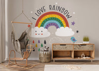 Kids nursery with rainbow wall mural and white wooden storage furniture on a rug.