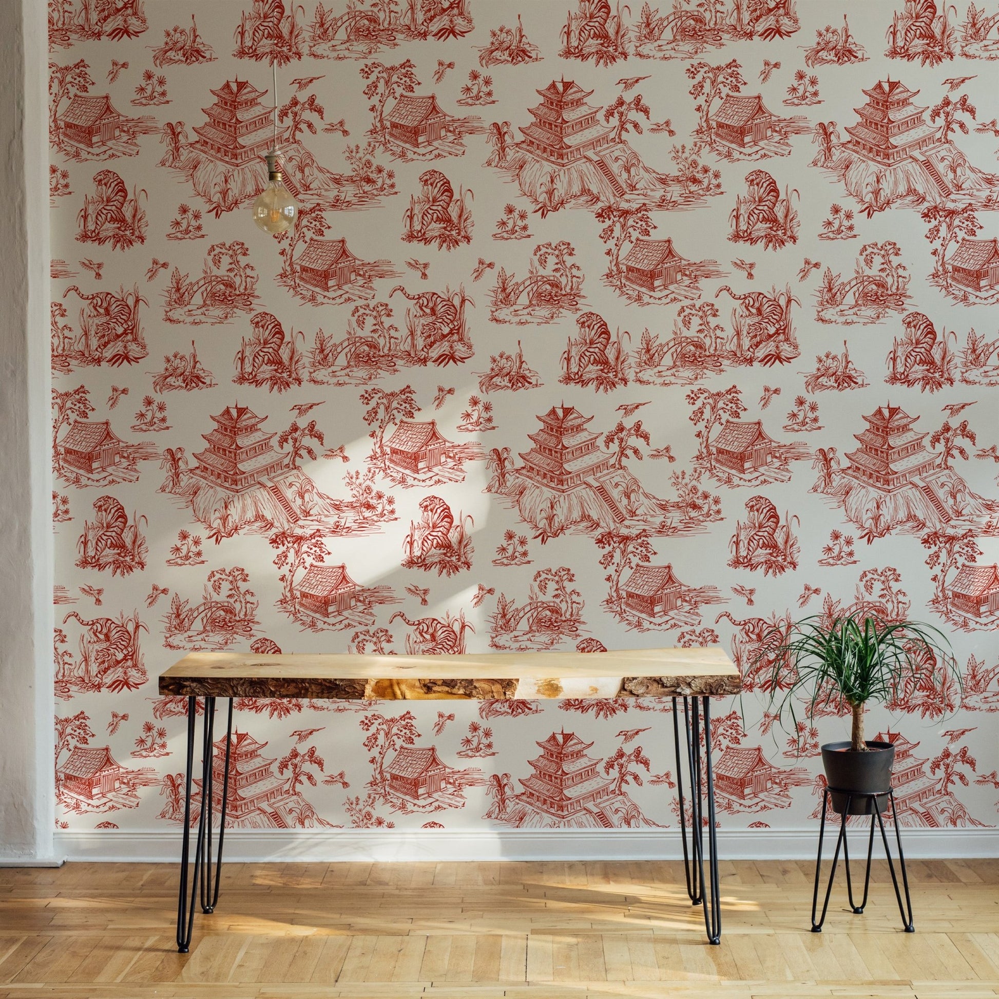 Red chinoiserie wallpaper in a home office with a minimalist desk and plants.