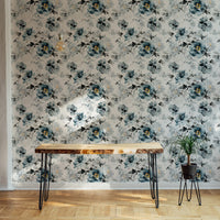 Blue indigo floral wallpaper behind a slim wooden desk and black metal chair.