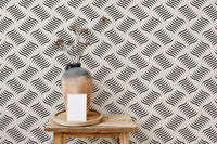 Monochrome ripple wallpaper behind a ceramic vase on a wooden stool.