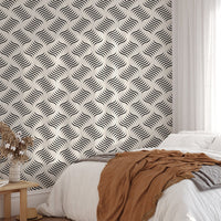 Monochrome ripple wallpaper behind a bed with a brown throw blanket.