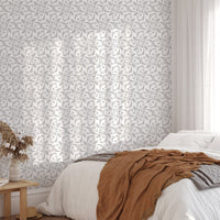 Damask pattern wallpaper on bedroom wall with white bedding and brown throw.