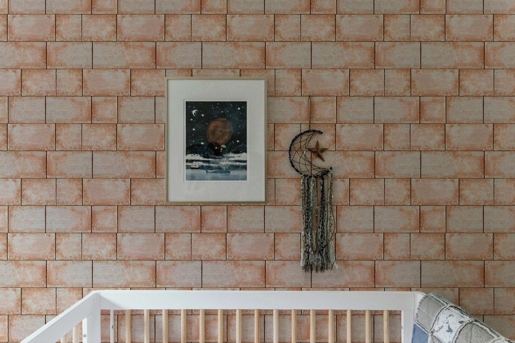 Sandstone wallpaper behind white nursery crib with framed artwork.