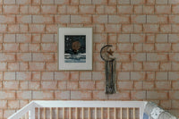 Sandstone wallpaper behind white nursery crib with framed artwork.