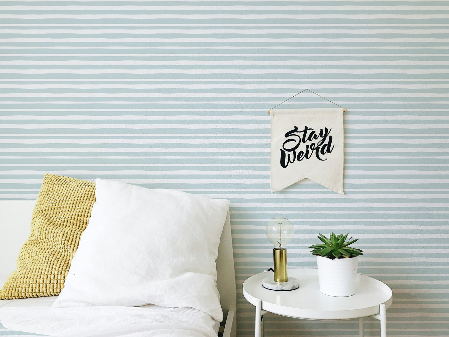 Bedroom setting with striped wallpaper and white bedding on a wooden bed frame.