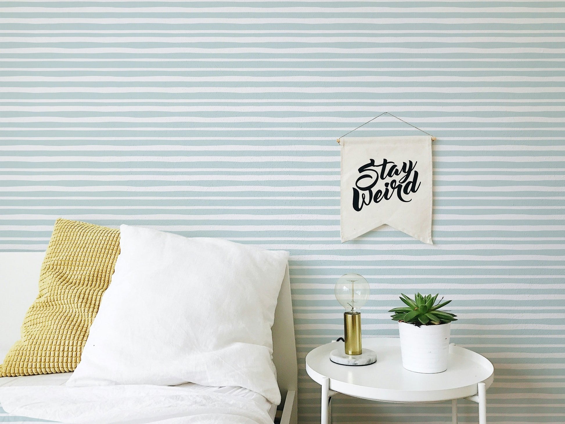 Bedroom setting with striped wallpaper and white bedding on a wooden bed frame.