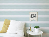 Bedroom setting with striped wallpaper and white bedding on a wooden bed frame.