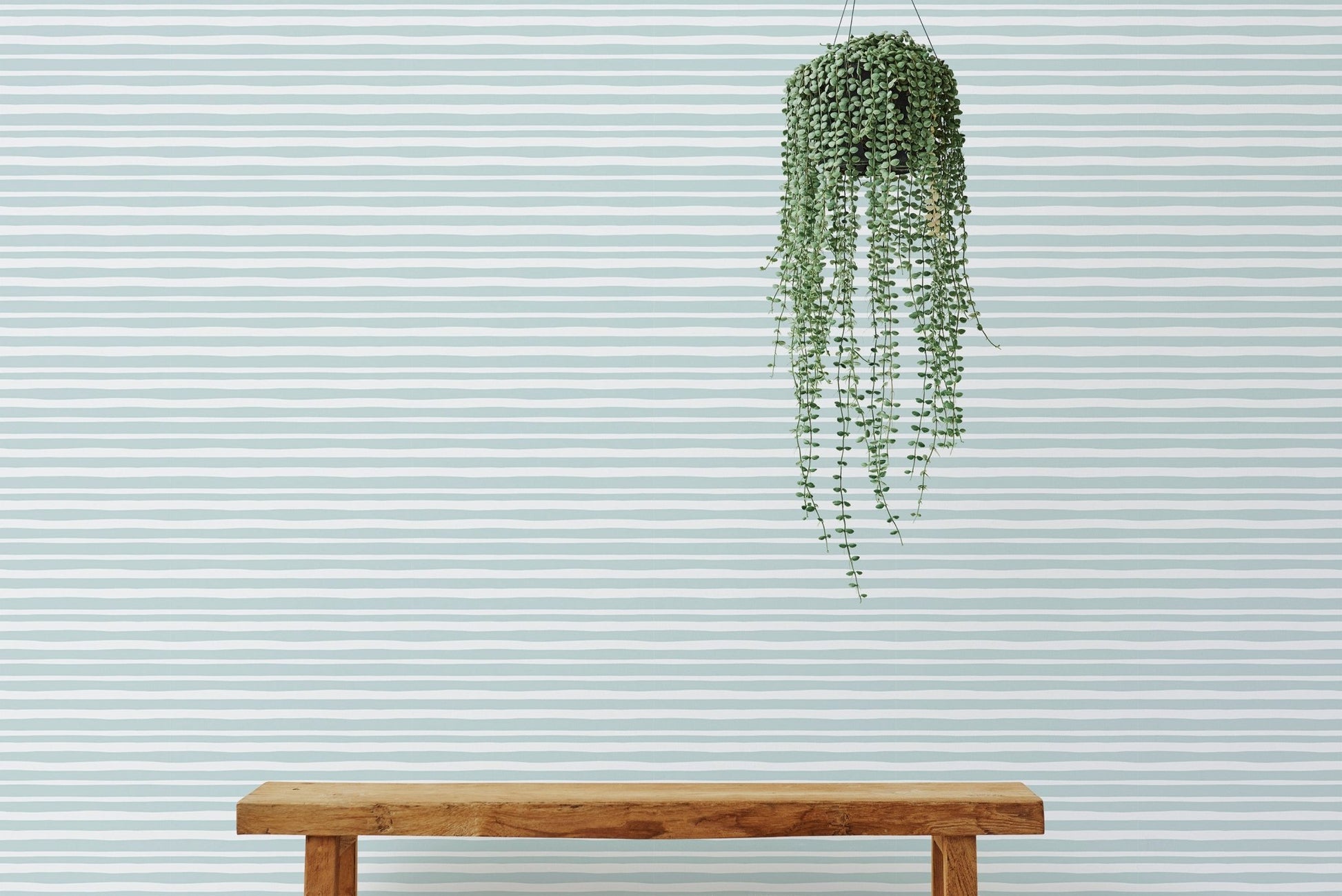 Simple wooden bench in front of a sea green horizontal striped wallpaper.