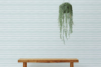 Simple wooden bench in front of a sea green horizontal striped wallpaper.