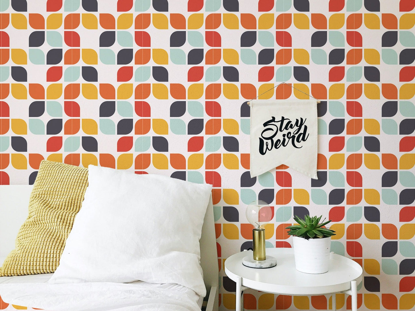 Abstract leaf shape tile wall mural behind a white bed with yellow and grey cushions.