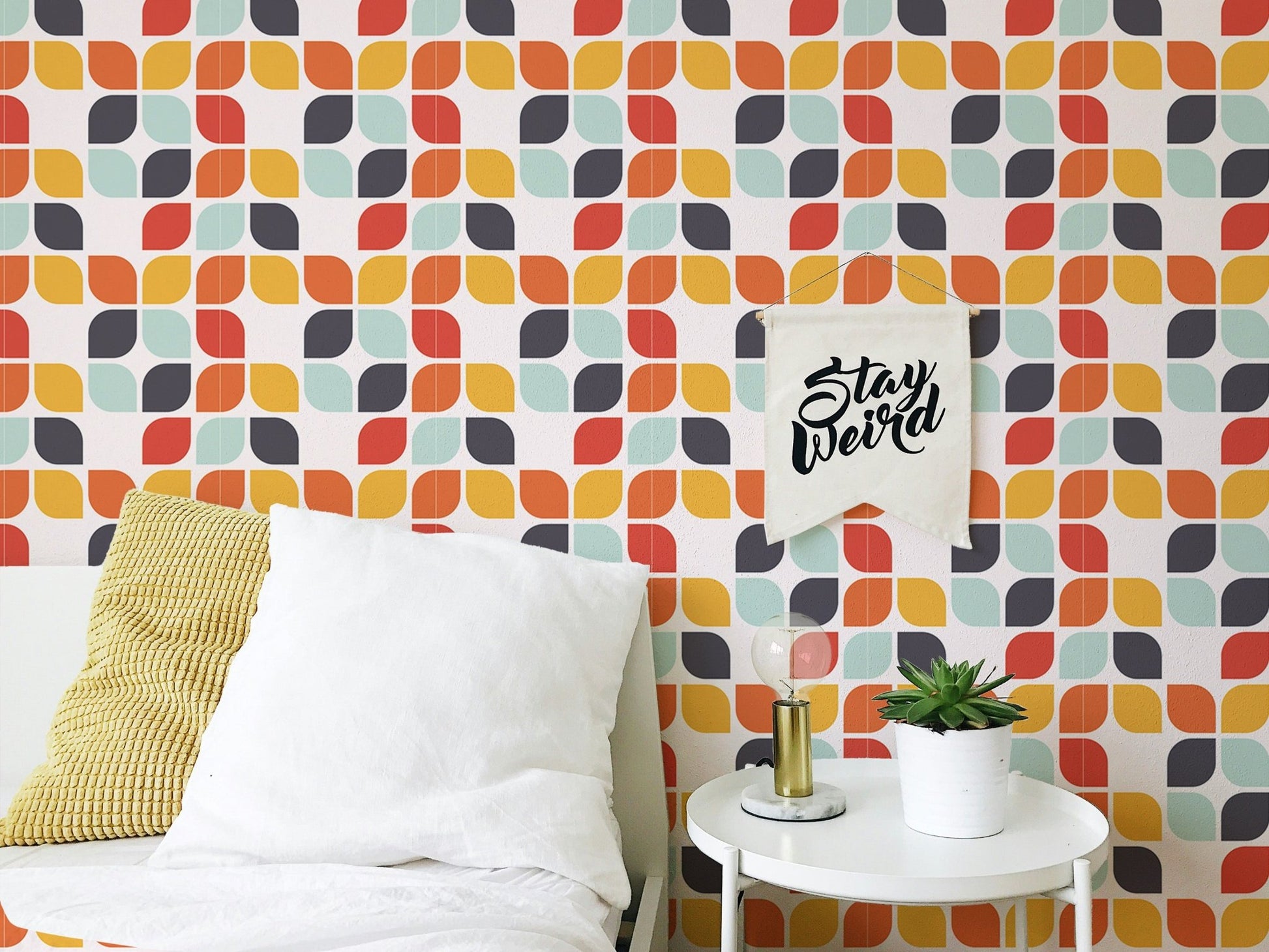 Abstract leaf shape tile wall mural behind a white bed with yellow and grey cushions.