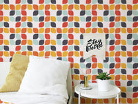 Abstract leaf shape tile wall mural behind a white bed with yellow and grey cushions.