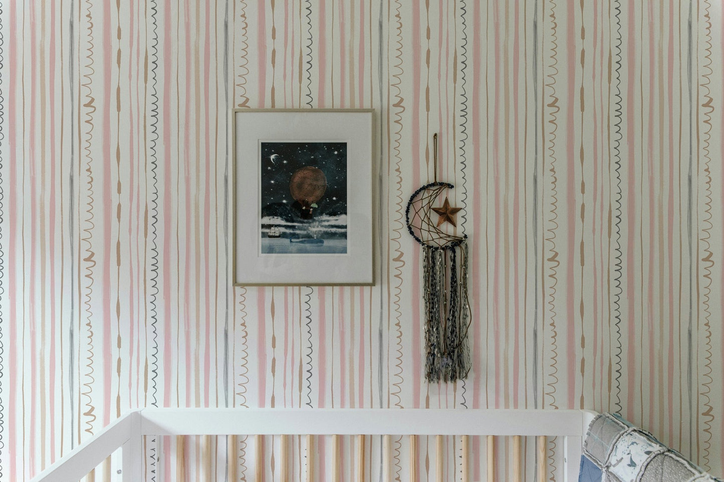 Pink and beige vertical striped wallpaper in a nursery with a white crib and artwork.