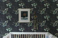 Dark floral wallpaper with green leaves in a minimalist nursery above a white crib.