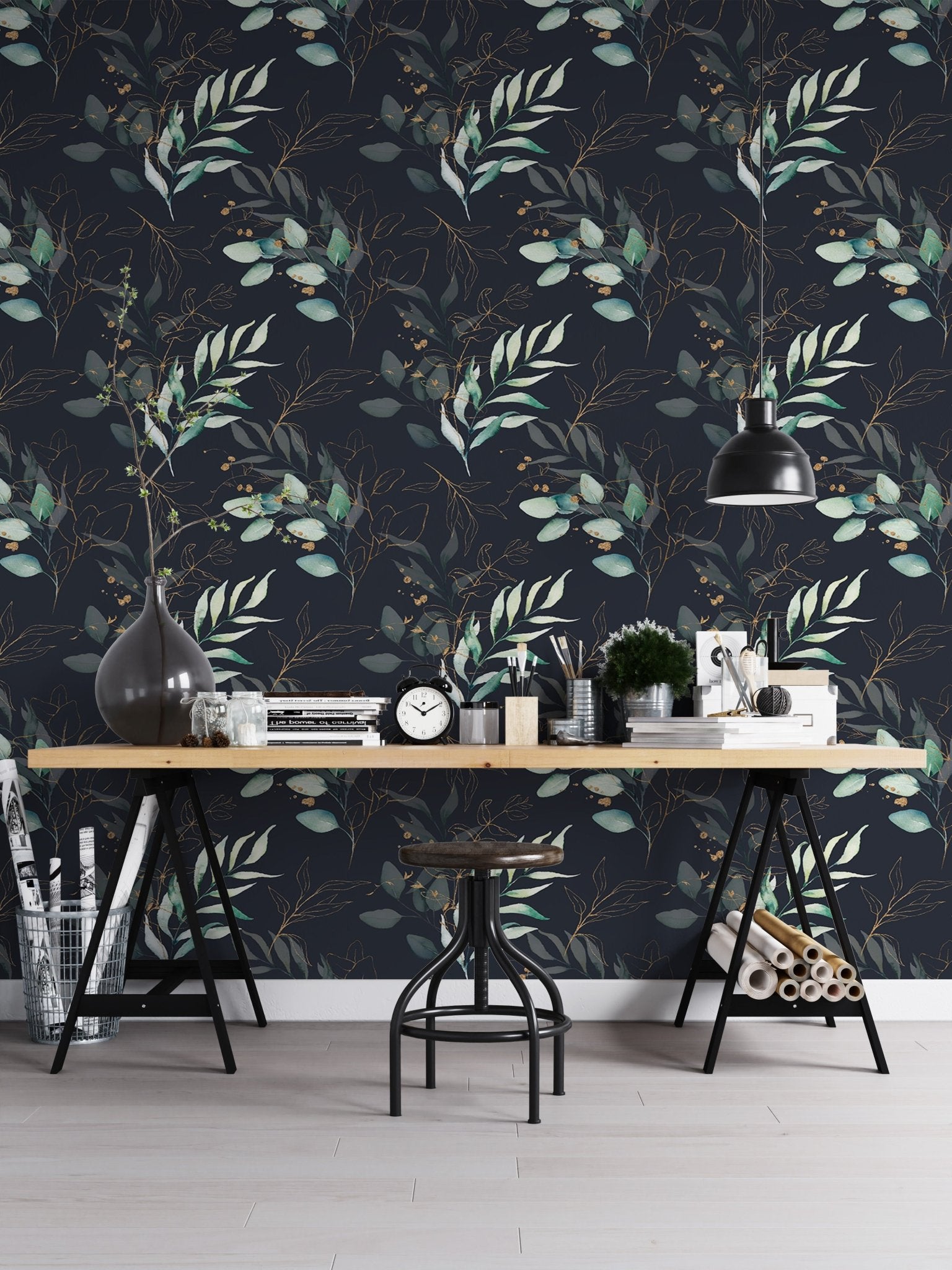 Dark botanical leaves wallpaper used as a backdrop for a home office desk and black chair.
