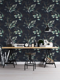 Dark botanical leaves wallpaper used as a backdrop for a home office desk and black chair.