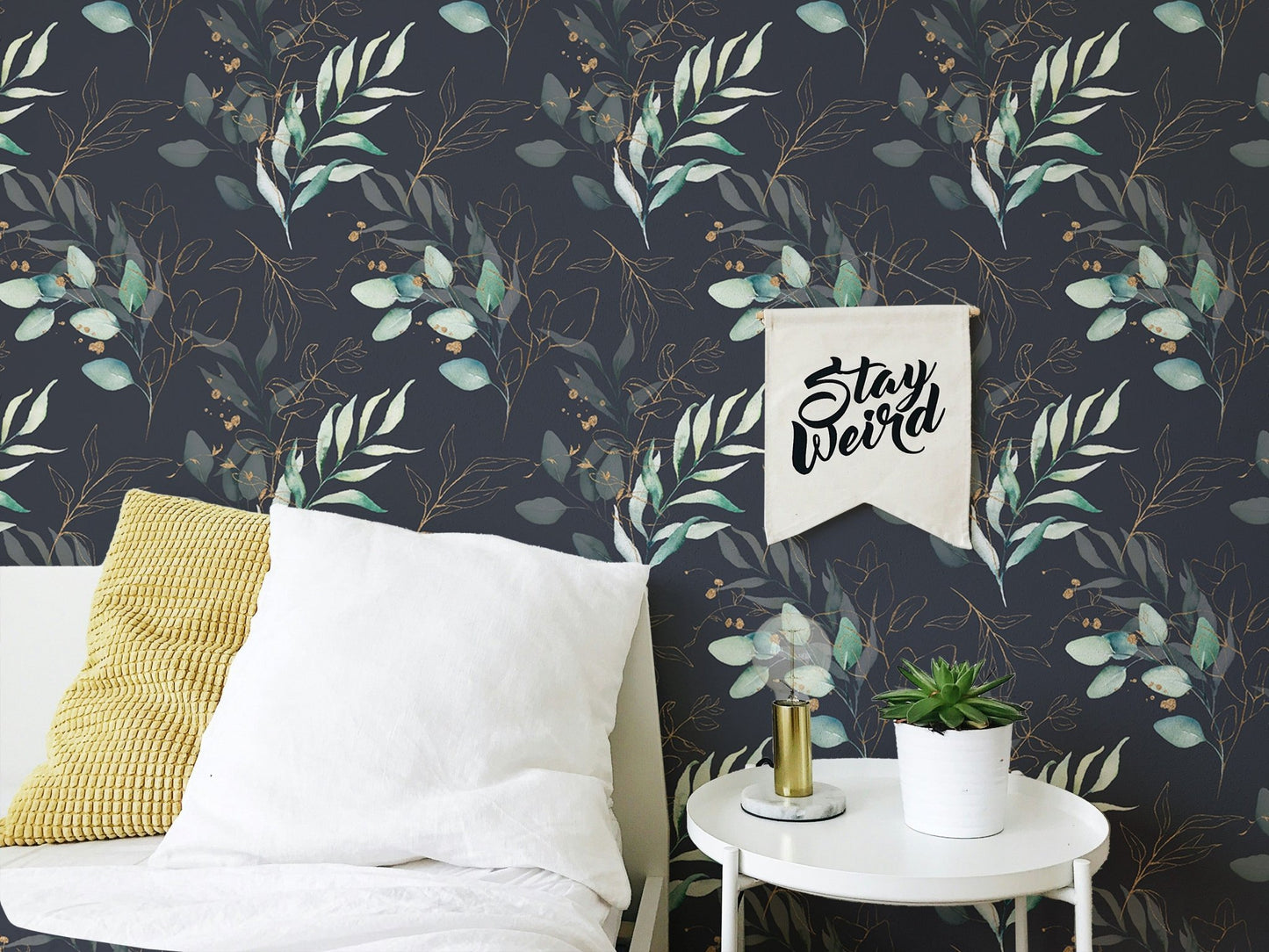 Dark floral wallpaper on a bedroom wall featuring a white framed picture and yellow pillow.